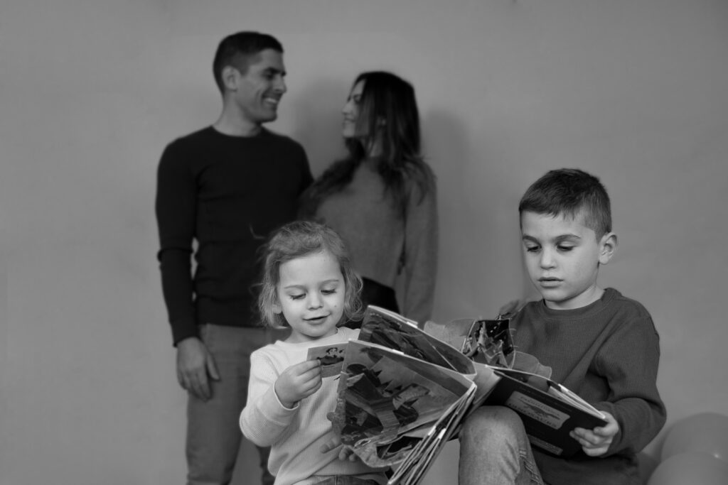 The Family Photographer Chicago Experience, 2 kids reading a book while the parents are in the background smiling at each other